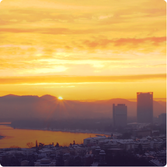 Sonnenaufgang über einer Stadt mit Fluss und Bergen im Hintergrund, mit gelbem Himmel.